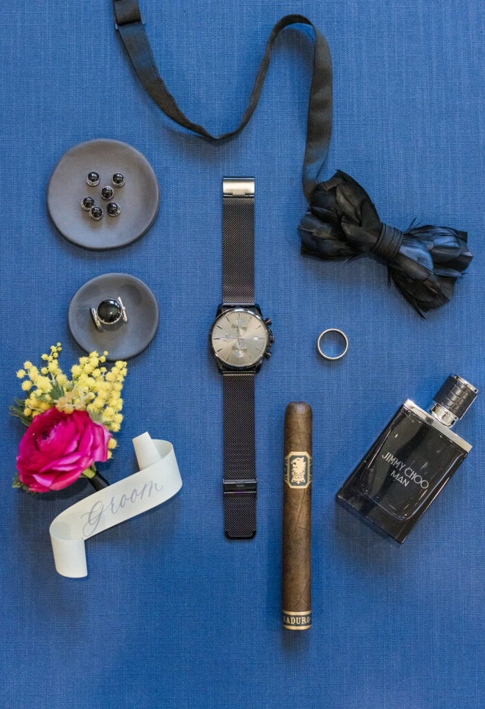 groom wedding flat lay with cologne, vibrant florals and jewelry