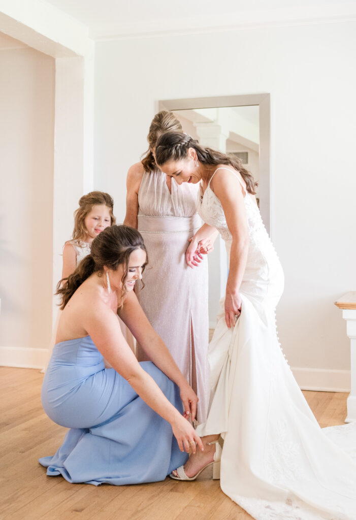 Bride's sister assisting bride with putting on her shoes occurs at the beginning of a wedding photography timeline.