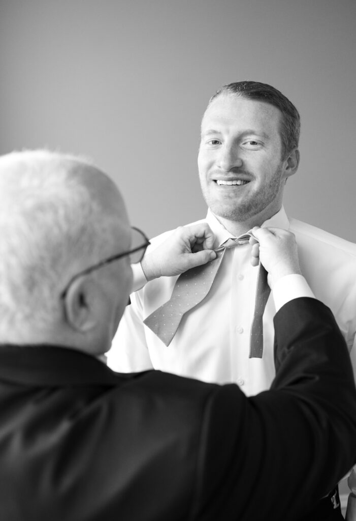 A father tying son's bow-tie at the beginning of a wedding timeline